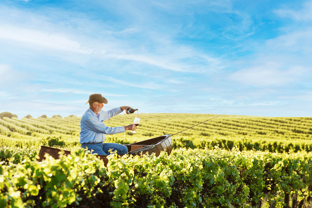 Winemaker sitting in a canoe atop the vines, pouring wine into a glass.