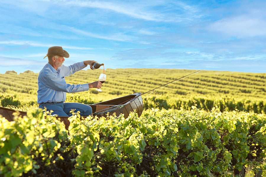 A man sitting in a canoe atop a vineyards pours wine into a glass